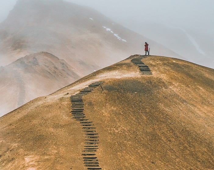 Person auf einer Bergspitze die er über einen langen Pfad erreicht hat